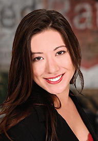 A professional headshot of a smiling woman in a dark blazer.