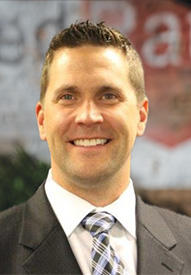 A professional headshot of a smiling man in a suit.